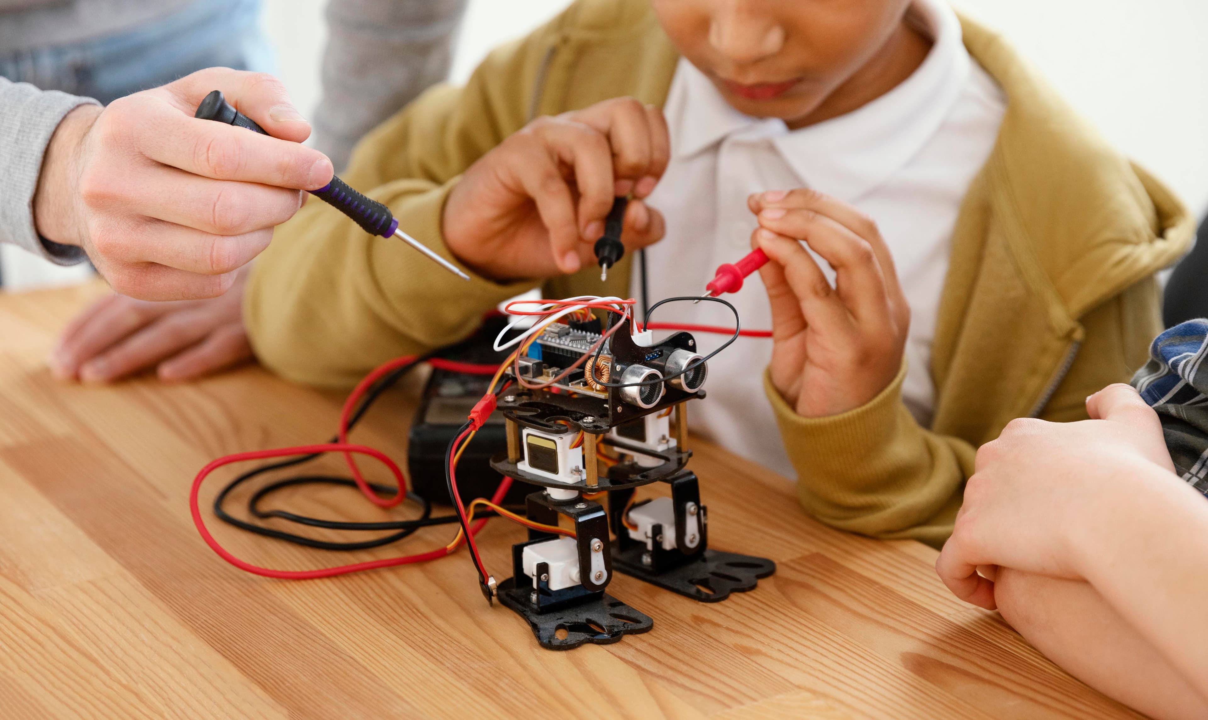 Students using a screwdriver and probes to assemble an electronic robot during a workshop